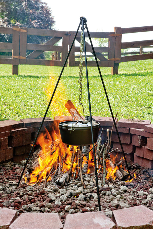Tripod being used to hold dutch oven over fire in firepit.