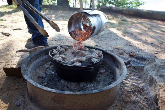 Someone emptying hot coals onto Dutch oven while cooking outside.