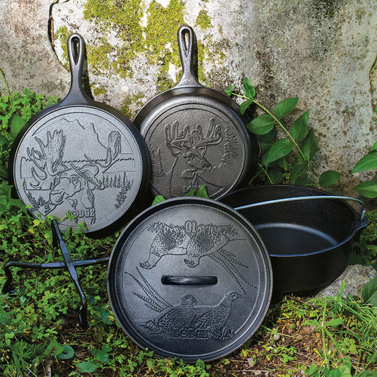 A set of seasoned cast iron cookware including a skillet, griddle, and a camp dutch oven with engraved wildlife designs, displayed on a natural stone background.