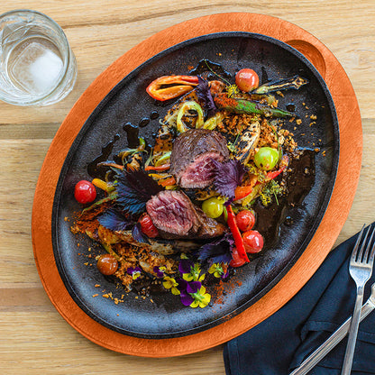 Delicate dish of beef with vegetables on a cast iron serving griddle with an orange underliner, served on a kitchen table.