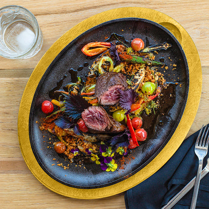 Delicate dish of beef with vegetables on a cast iron serving griddle with a yellow underliner, served on a kitchen table.