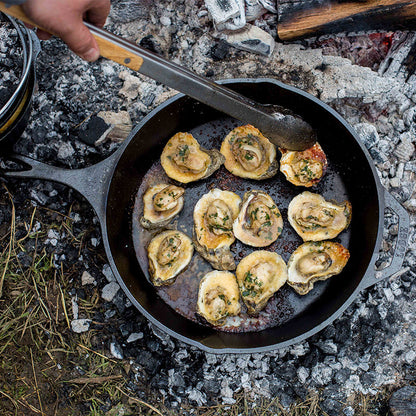 Someone turning mussels as they roast in skillet at campfire.