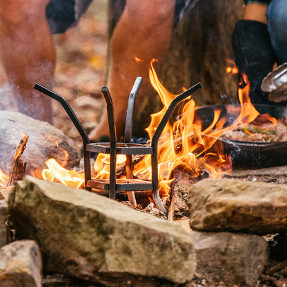 Stand sitting in campfire after being used to cook steak with skillet.