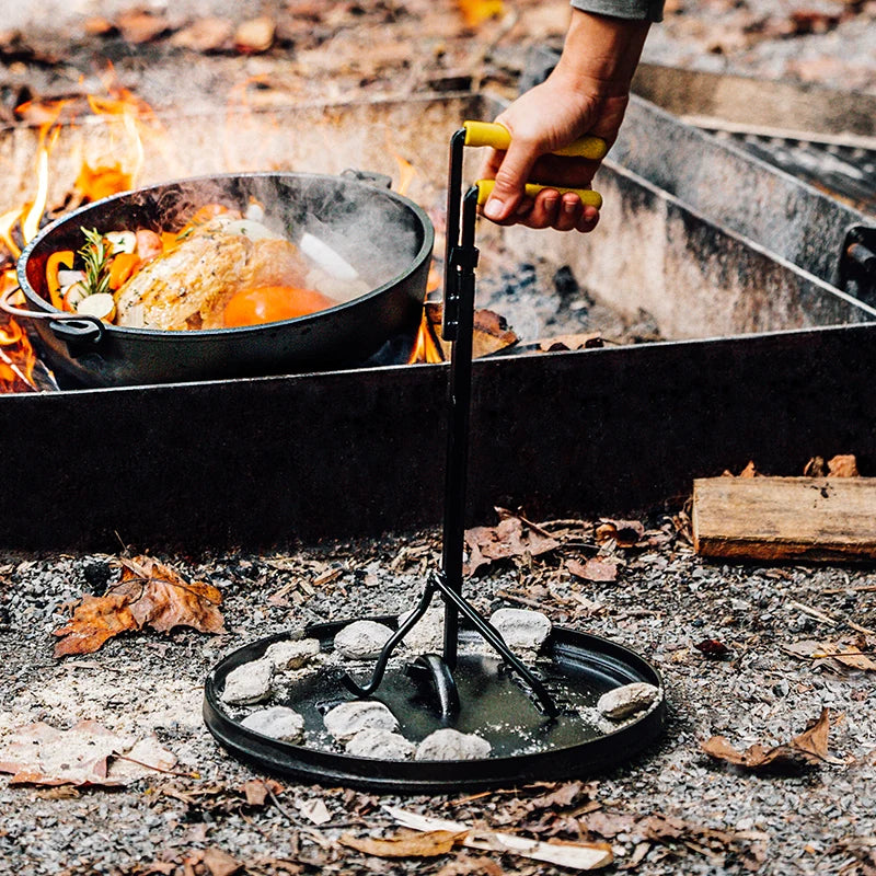Someone moving lid away from fire while food cooks in dutch oven.