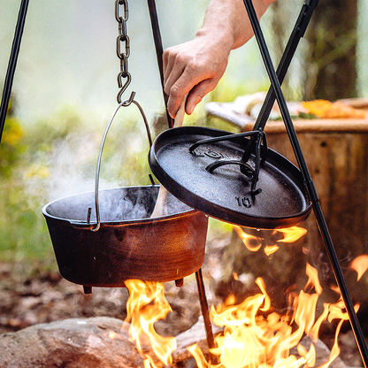 Someone stirring a meal in the dutch oven hanging over fire.