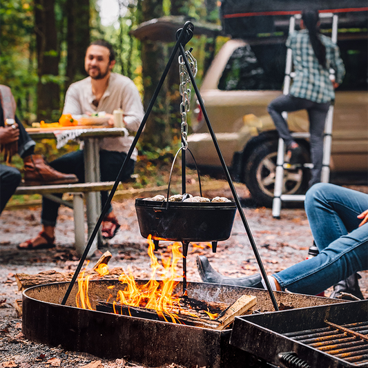 Tripod being used to hold dutch oven over fire at campsite.