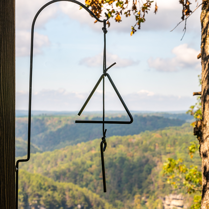 Triangle bell hanging on a porch in front of mountain view.