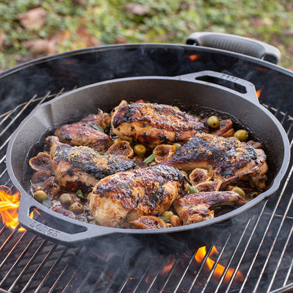 Chicken and olives being cooked in pan on a charcoal grill.