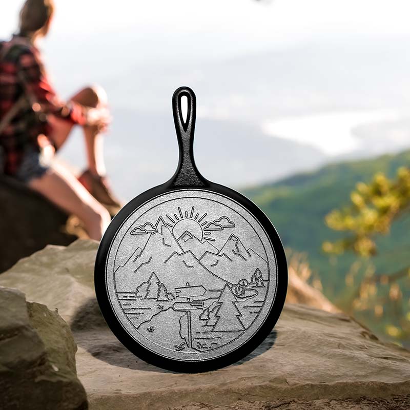 Cast iron skillet with mountain design on a rock with a blurred person and scenic background