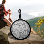 Cast iron skillet with mountain design on a rock with a blurred person and scenic background