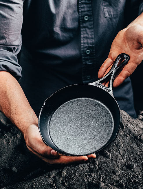 Someone holding skillet in front of a pile of ground iron.
