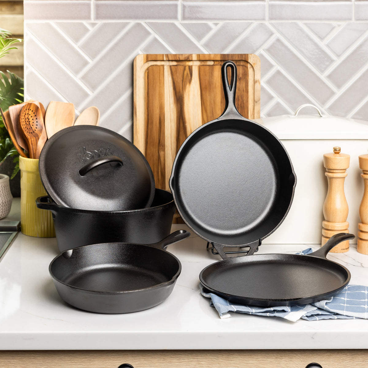 Set of black cast iron cookware on a kitchen counter with a tiled backsplash.