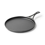 Black circular griddle with a long handle and shallow edges.