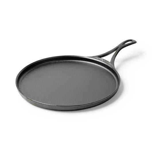 Black circular griddle with a long handle and shallow edges.