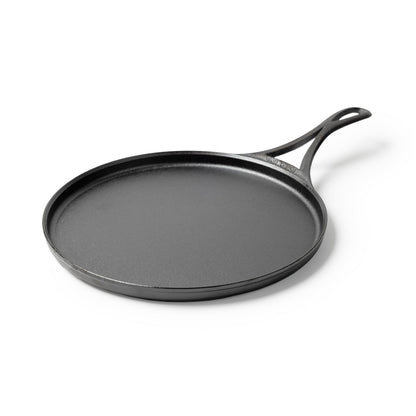 Black circular griddle with a long handle and shallow edges.