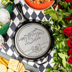 Seasoned Cast Iron Kentucky Derby Skillet for the 152nd year, placed on checkered table surrounded by food and roses.