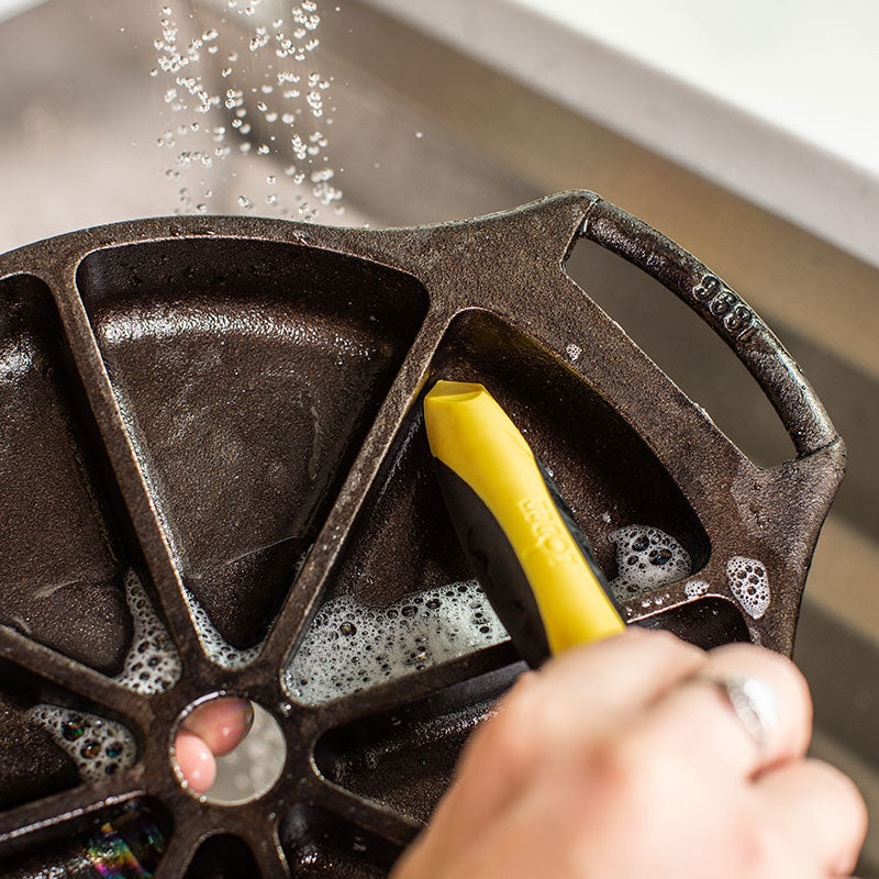 Someone using pointed end of brush to clean the corners of the wedge pan.