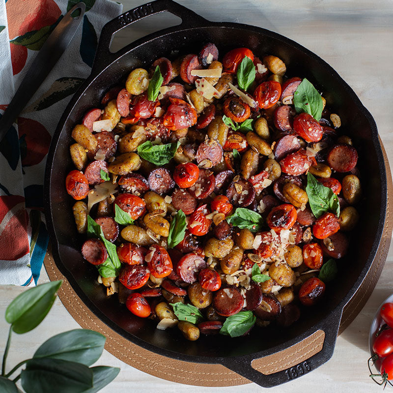 Top view of dish with sausage, tomato's, potato's, and basil ready to serve on counter.