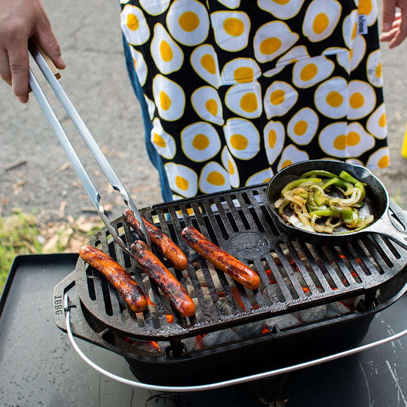 Someone cooking hot dogs on our Sportsman's Pro Grill using tongs.