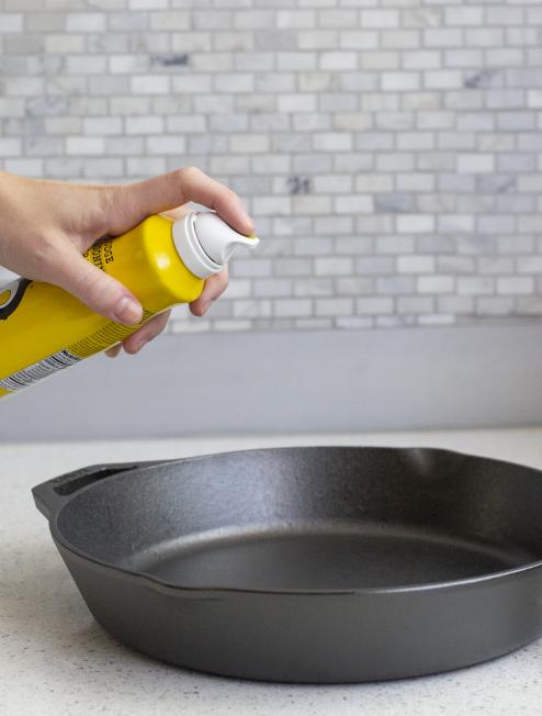 Someone spraying seasoning oil on skillet.