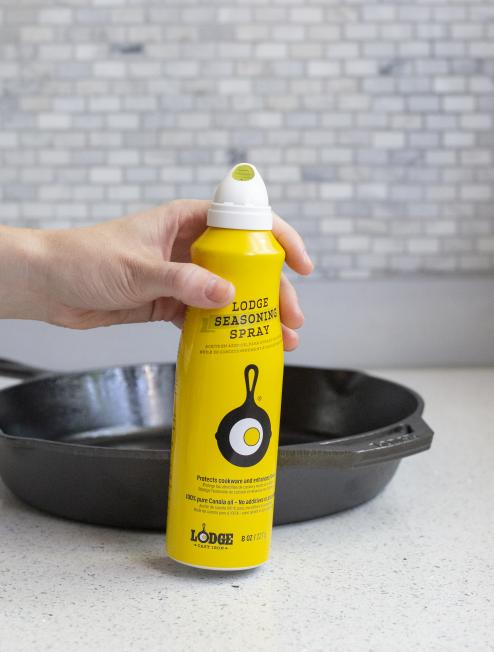 Someone holding spray in front of skillet.