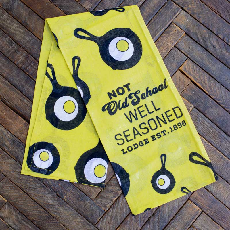 Towel placed on wooden surface, partially unfolded to show the Lodge skillet and egg logo scattered throughout.