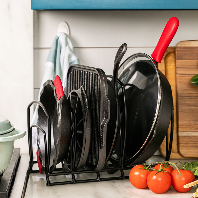 Storage rack on kitchen counter organizing our pie pan, wedge pan, single burner griddle, round griddle, and skillet with a glass lid.