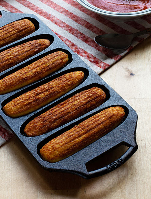Freshly baked cornbread shaped like corn, served and prepared in pan.