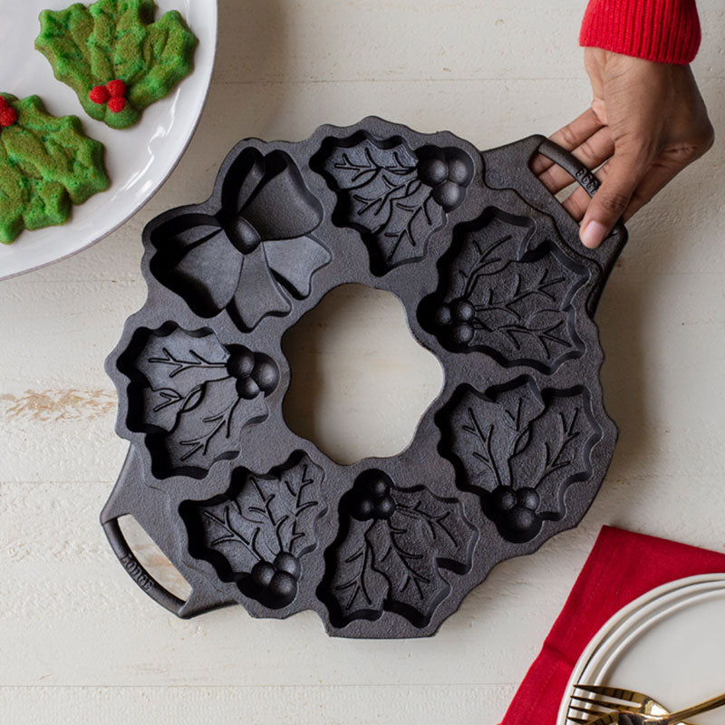 Someone placing pan near baked cookies, colored to match mistletoe shape.