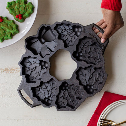 Someone placing pan near baked cookies, colored to match mistletoe shape.