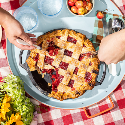 People eating strawberry pie from pan on a checkered tablecloth with a bowl of apples and a glass of water.