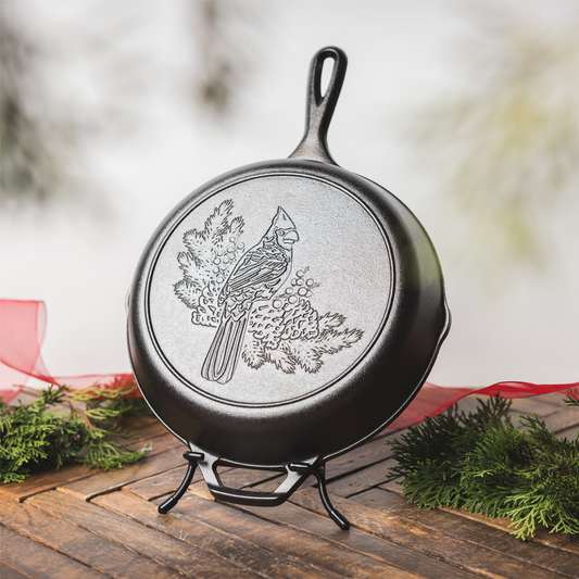 Cast iron skillet with a cardinal engraving, displayed on a Lodge Skillet Display stand with a festive holiday background.