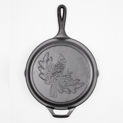 Cast iron skillet with a Cardinal engraved on the back who is perched on balsam fir branches.