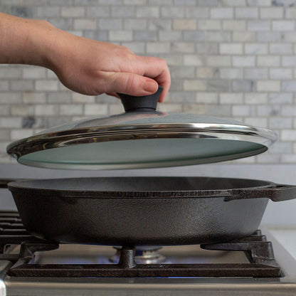 Someone placing lid on skillet while cooking on stove.