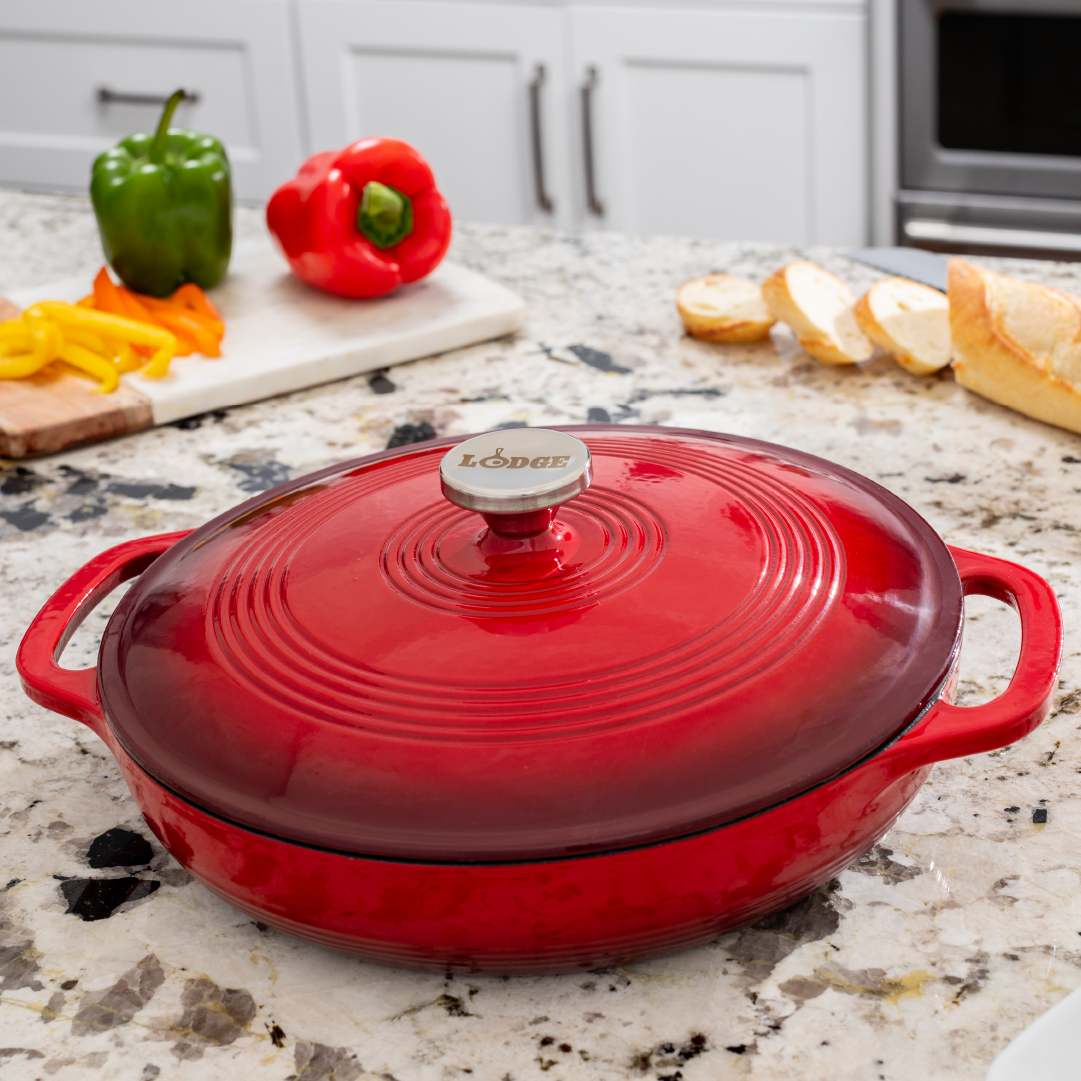 Braiser on kitchen counter in front of fresh peppers and sliced bread.