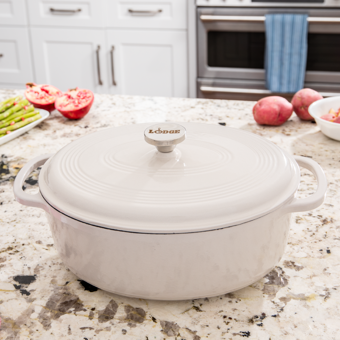 A white enameled cast iron Dutch oven with a lid and metal handles, displayed in a kitchen setting.