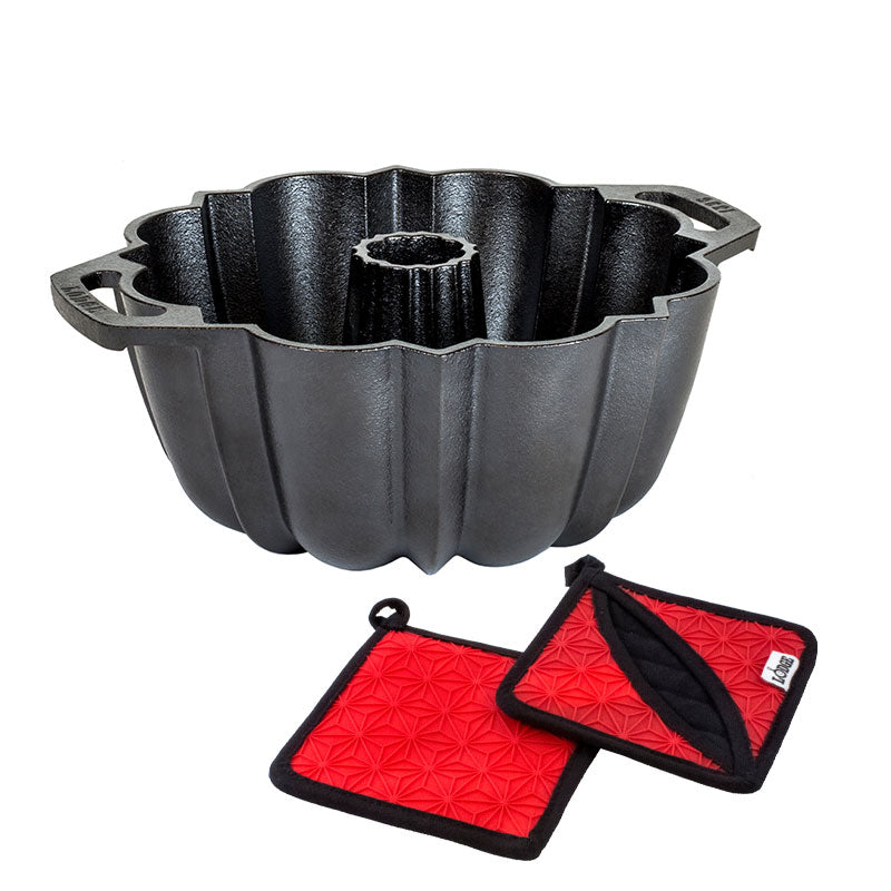 A black cast iron fluted cake pan with two red silicone and fabric potholders.