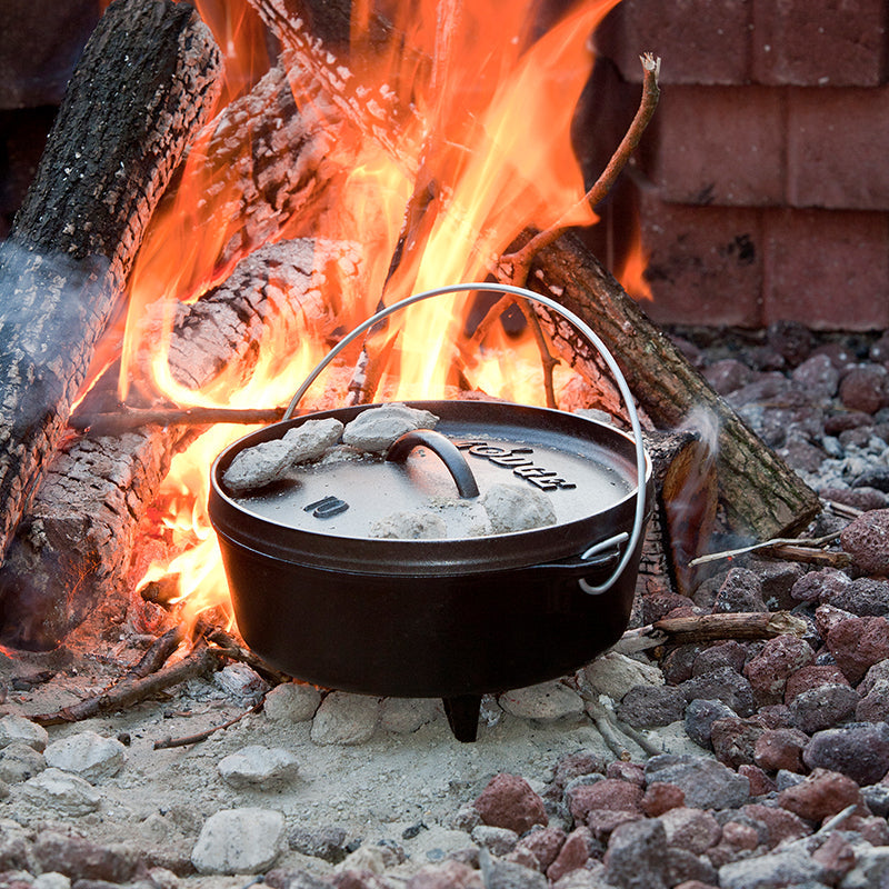 Dutch oven cooking near fire with coals on top.