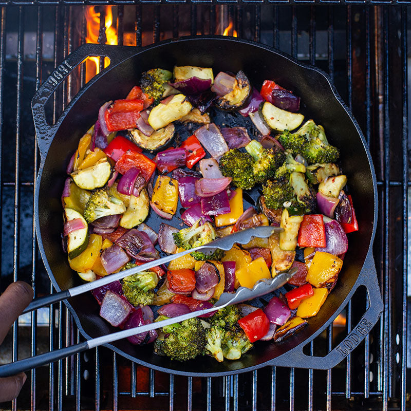 Someone turning vegetables while they roast on grill.