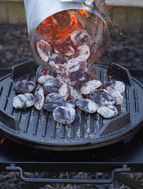 Someone using the charcoal chimney starter to dump hot coals into grill.