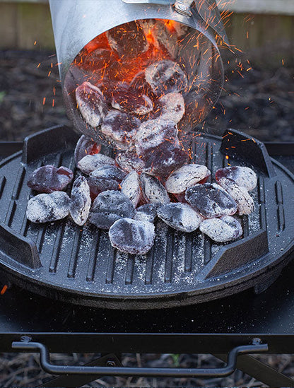Someone using the charcoal chimney starter to dump hot coals into grill.