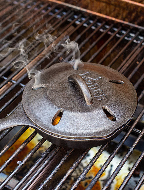 Smoker skillet on grill releasing smoke.