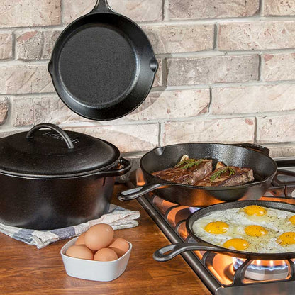 A set of black cast iron cookware including a pot, pan, grill pan, sauté pan, and a skillet, displayed on a stovetop with food being cooked in the pans and a seasoned cast iron label visible.