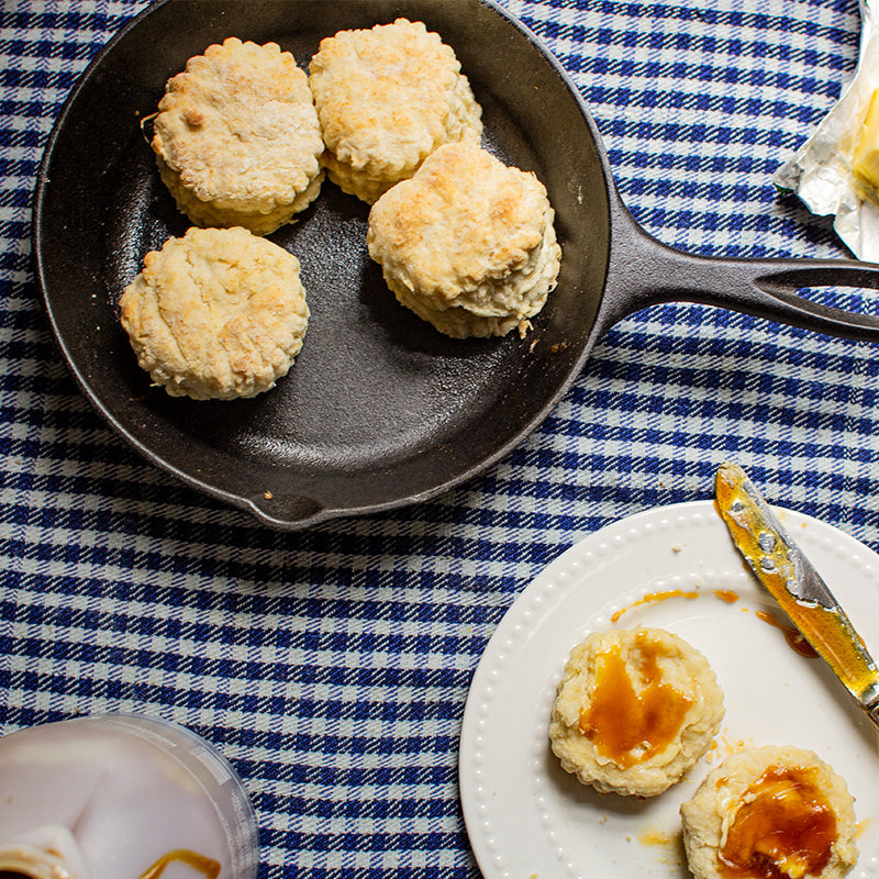 Freshly made biscuits in skillet near served biscuits with butter and jam.