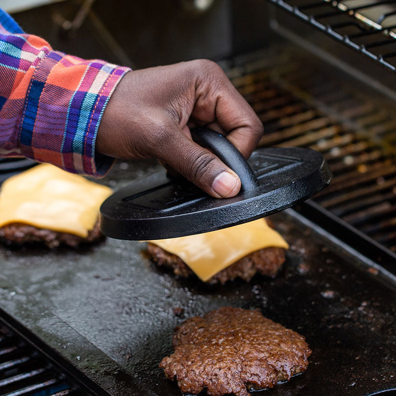 Someone using press on a burger patty to make Smash Burgers.