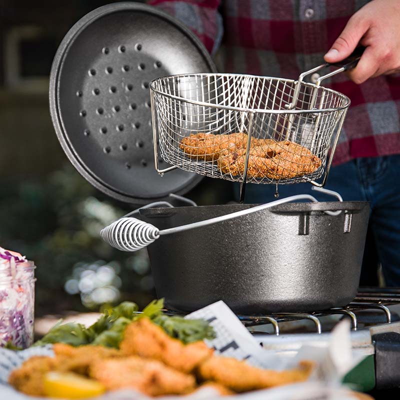 Someone taking basket out of dutch oven with freshly fried chicken.