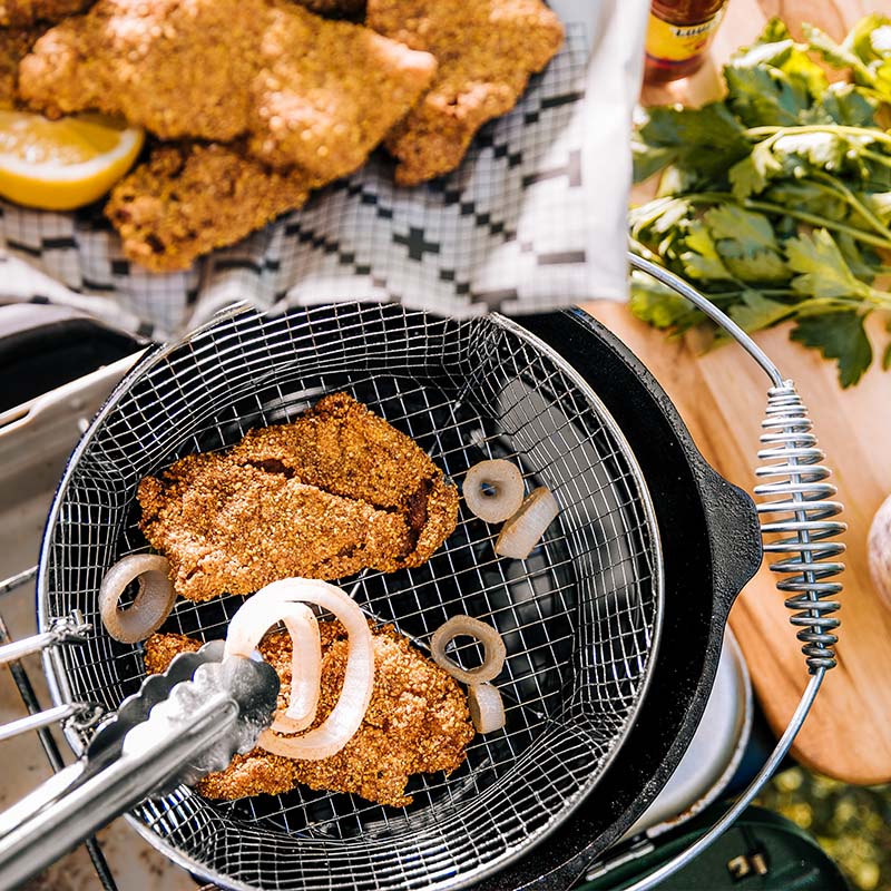 Someone placing onion rings into basket with chicken to fry.