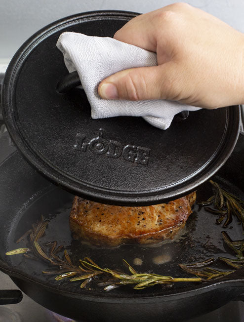 Someone using press on steak cooking on skillet.
