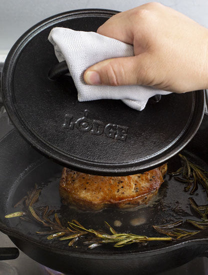 Someone using press on steak cooking on skillet.