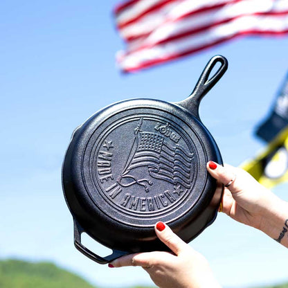 A person holding a 10.25 inch seasoned cast iron skillet with an embossed American flag design.